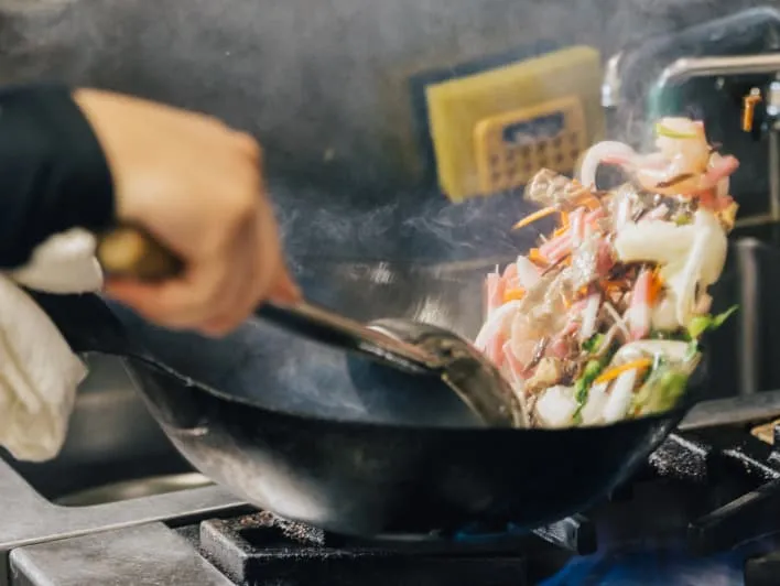 ガスコンロで野菜と肉を中華鍋で炒めている様子。